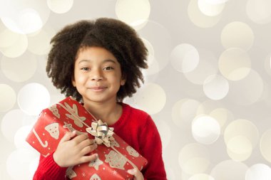 Gülümseyen, kıvırcık saçlı küçük bir kızın portresi. Elinde bir Noel hediyesi var. 