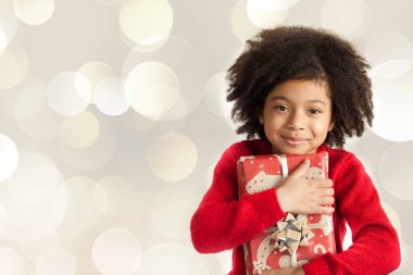 Gülümseyen, kıvırcık saçlı küçük bir kızın portresi. Elinde bir Noel hediyesi var. 