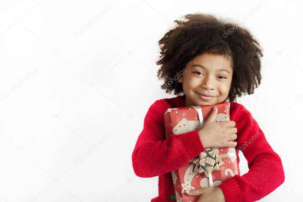 portrait of a smiling little girl with curly hair holding a Christmas gift 