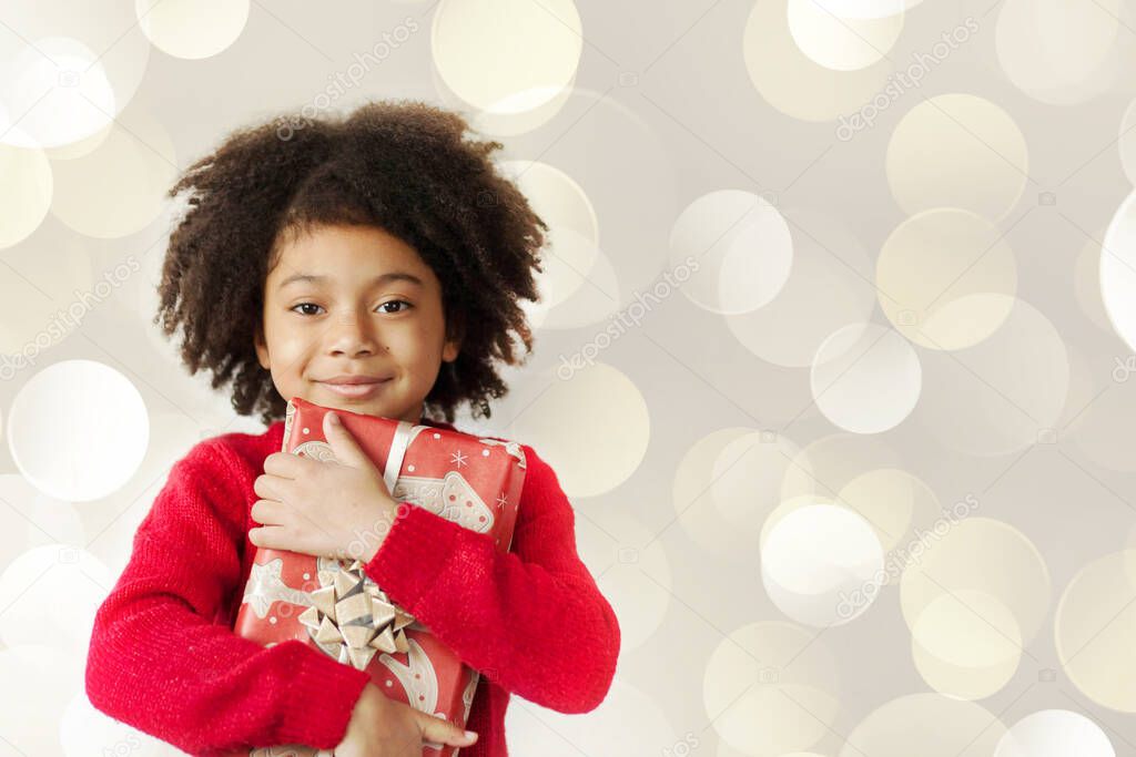 portrait of a smiling little girl with curly hair holding a Christmas gift 