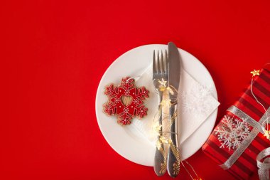 Kırmızı arka planda dekoratif sembollerle çizilmiş Noel masası servis ediliyor.