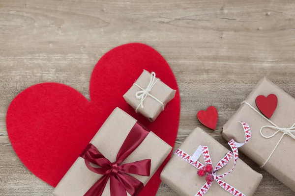 Aşk konsepti. Vlentine Günü. Saten kurdeleli kutular, hediyeler ve ahşap arka planda kırmızı büyük kalp..