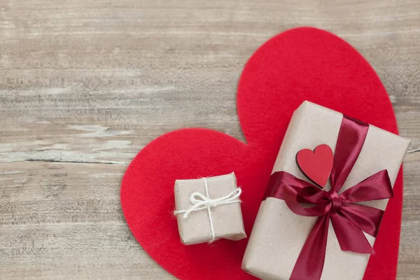 Aşk konsepti. Vlentine Günü. Saten kurdeleli kutular, hediyeler ve ahşap arka planda kırmızı büyük kalp..