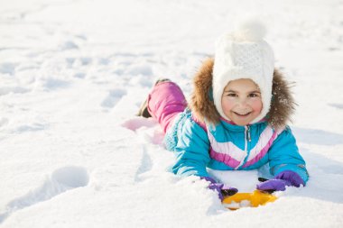 Kışlık elbiseli küçük kız parkta karla oynuyor. 