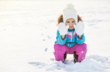 Kışlık elbiseli küçük kız parkta karla oynuyor. 