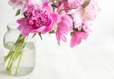 Ahşap arka planda cam vazoda pembe şakayıklar.