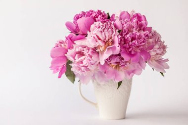 Beyaz arka planda vazoda pembe şakayıklar.