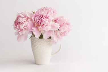 Beyaz arka planda vazoda pembe şakayıklar.