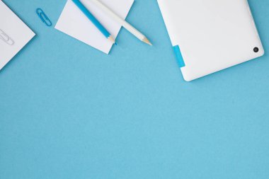 Mavi arkaplanda kırtasiye malzemesi ve not defteri olan ofis masasının üst görünümü