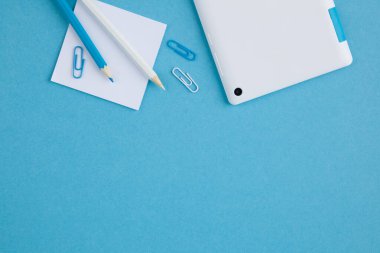 Mavi arkaplanda ataç ve kırtasiye malzemelerinin üst görünümü