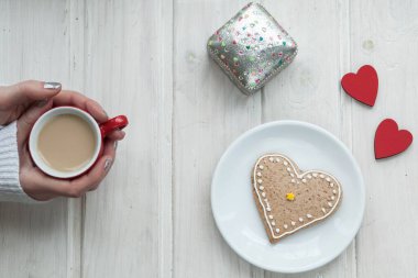 Bir fincan kahve ve kalp şeklinde kurabiyeler ahşap arka planda.