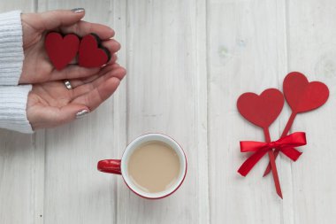 Ahşap arka planda bir fincan kahve ve hediye kutusu tutan eller.