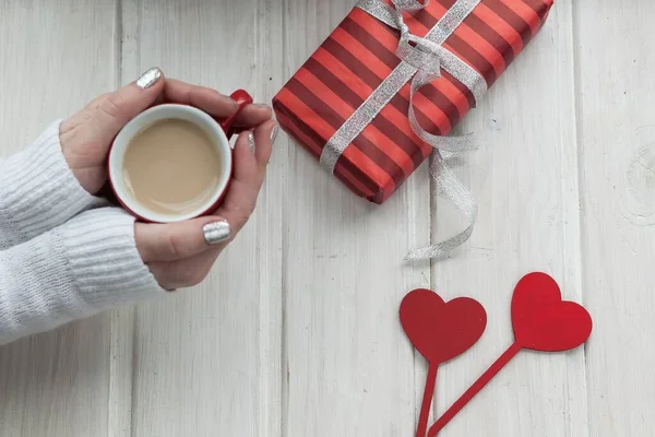 woman holding cup of coffee and gift box on wooden table