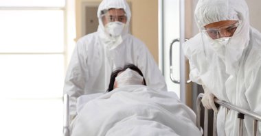 Asyalı hemşire ve doktor takım elbise ve yüz maskesi takarak sedye yatağı ve ciddi şekilde enfekte olmuş koronavirüs ya da kovid 19 hastası hastanedeki karantina odasına itiyorlar..