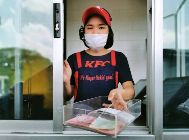 Bangkok, Tayland - 14 Haziran 2021: Coronavirus salgınını veya covid-19 virüs salgınını korumak için hijyen maskesi takan servis servis görevlisi KFC fast food kasiyeri müşteriye para değişimi sağlıyor.
