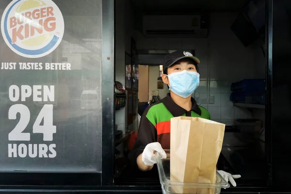 Bangkok, Tayland - 3 Eylül 2020: Burger King fast food kasiyeri Coronavirus salgınını veya covid-19 salgınını korumak için maske takarak servis yoluyla müşteriye kağıt torba içinde hamburger verdi.