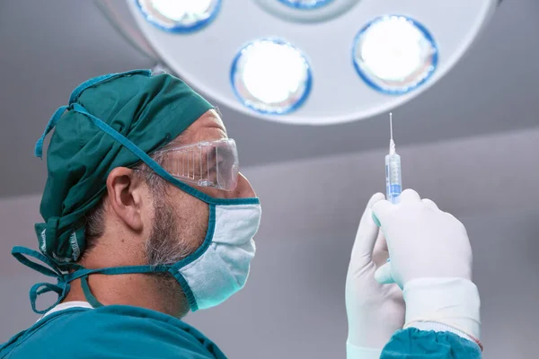 Hastanenin ameliyathanesinde ameliyat öncesi genel anestezi ilacı ya da antiviral ilaç şırıngası tutan profesyonel bir doktor..