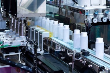 Kozmetik ve cilt bakımı ürünlerinde otomatik kaplama ve etiketleme makinesinin taşıyıcı bandı üzerinde hareket eden beyaz plastik şişe. Kozmetik endüstrisi ve ai teknoloji makineleri konsepti.