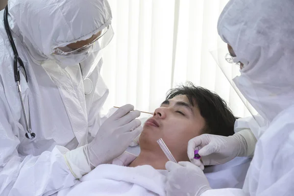Erkek hemşire ve doktor takım elbise ve yüz maskesi giyip Coronavirus COVID-19 PCR testi yapıyorlar. Hasta nazal NP ve oral OP örnek toplama süreci, viral rt-PCR DNA tanılama prosedürü.