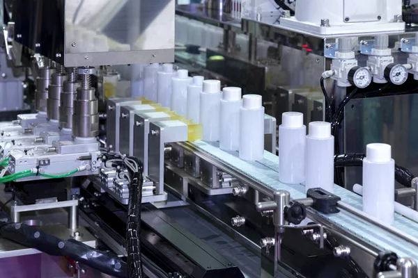 Kozmetik ve cilt bakımı ürünlerinde otomatik kaplama ve etiketleme makinesinin taşıyıcı bandı üzerinde hareket eden beyaz plastik şişe. Kozmetik endüstrisi ve ai teknoloji makineleri konsepti.