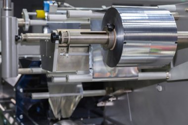 Yiyecek üretim fabrikasındaki otomatik paketleme makinesinde yiyecek ambalajı için alüminyum folyo rulosu. sanayi ve teknoloji kavramı. 