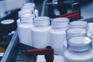 Tıbbi fabrikadaki dolum makinesinin üretim hattındaki beyaz plastik şişe. seçici odak.