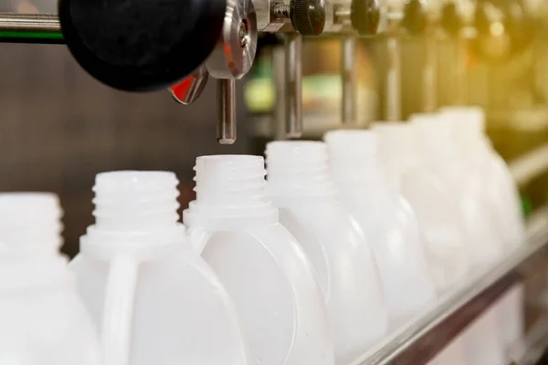 Fabrikadaki konveyörün üretim hattındaki beyaz plastik galonlar ya da şişeler sabahları güneş ışınıyla dolduruluyor. Seçici odaklanma. sanayi ve teknoloji kavramı. 
