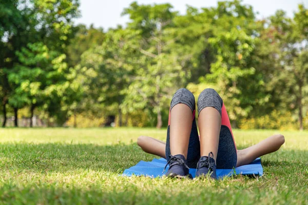 young teen women in sport suit lay down to sleep and relaxing on the green grass in the park after running exercise in summer morning with warm sunlight. people and lifestyle concept
