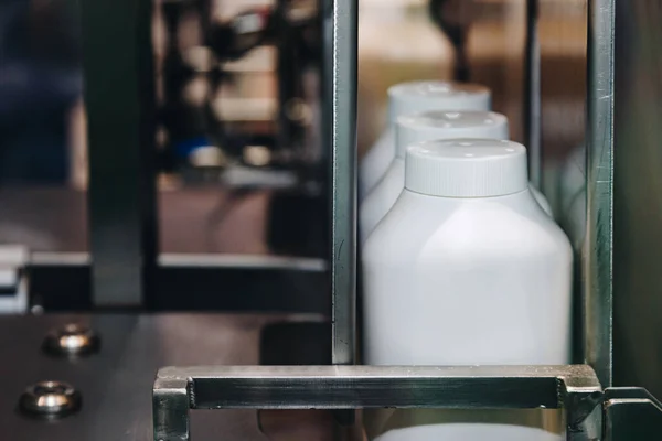 Beyaz plastik bebek pudrası ürünleri konveyör bandında kozmetik fabrikasındaki paketleme makinesine taşınıyor..