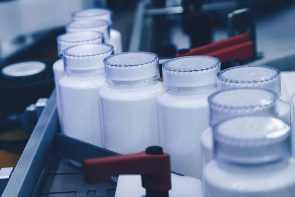 Tıbbi fabrikadaki dolum makinesinin üretim hattındaki beyaz plastik şişe. seçici odak.