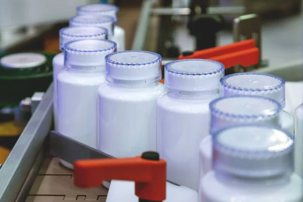 white medicine plastic bottle on production line of conveyor at filling machine in medical factory. selective focus. pharmaceutical manufacturing and industry concept.