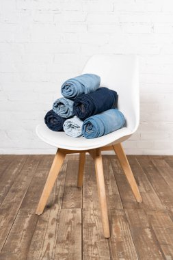 rolled denim garments on white chair placed on wooden floor near brick wall clipart