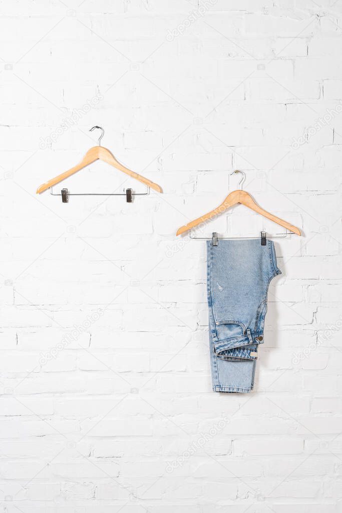 hangers and blue jeans near white brick wall