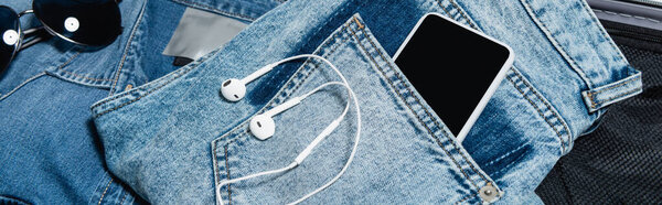 close up view of mobile phone in pocket of jeans near earphones and sunglasses, banner