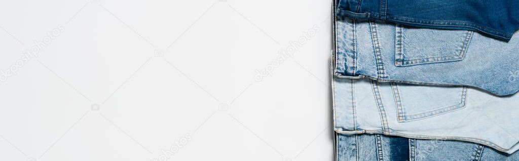vertical row of different blue jeans on white background, top view, banner