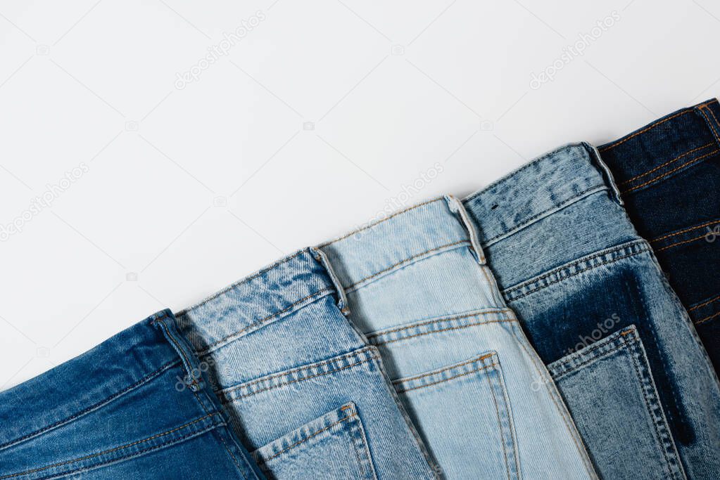 diagonal row of various jeans on white background, top view