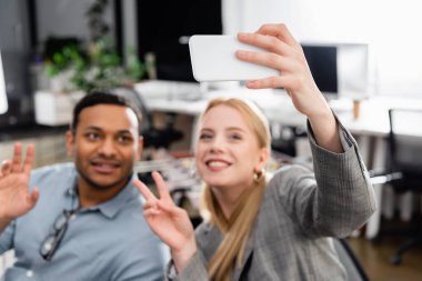 Sırıtkan iş kadınının Hintli meslektaşıyla bulanık arka planda selfie çektiği akıllı telefon. 