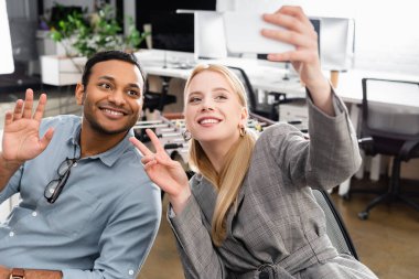 Gülümseyen çok ırklı iş adamları bulanık arkaplanda akıllı telefonlarıyla selfie çekiyorlar. 