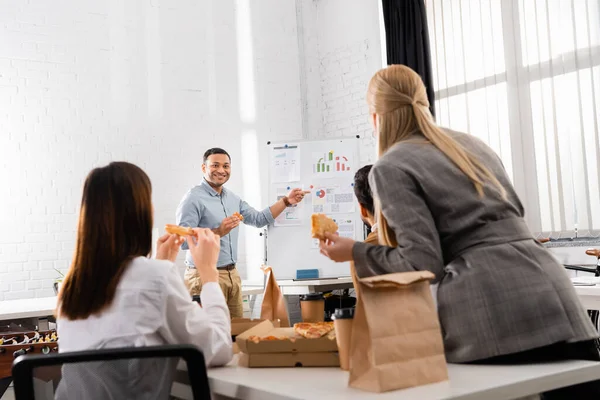 Smiling Indian Businessman Pizza Pointing Flipchart Colleagues Blurred Foreground Office — Stock Photo, Image