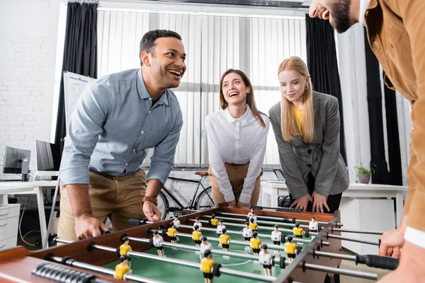 Positive multiethnic business people standing near table soccer in office