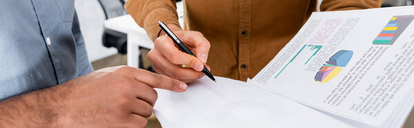 Cropped view of businessman pointing with finger near colleague with papers and pen in office, banner 