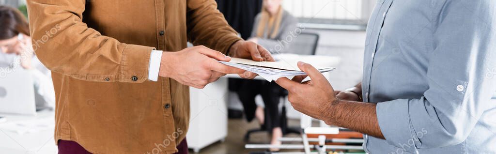 Cropped view of businessman giving paper folder to colleagues in office, banner 