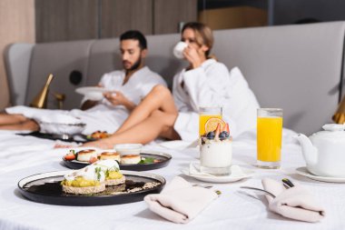 Lezzetli tatlılar ve portakal suyu. Yatakta, bir çiftin yanında. Otel odasındaki bulanık arka planda. 