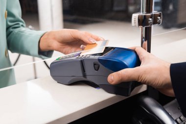 Ödeme terminali olan otel resepsiyonisti ve otel lobisinde kredi kartı olan bir kadın. 