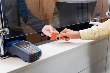 Otel lobisindeki ödeme terminalinin yakınındaki bir adama anahtar veren resepsiyonist görüntüsü. 