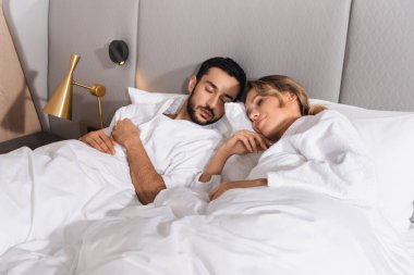 Otelde beyaz yatakta uyuyan ırklar arası genç bir çift. 