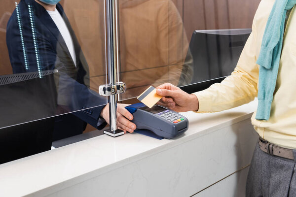 Обрезанный вид человека, платящего кредитной картой рядом с менеджером с платежным терминалом в отеле 