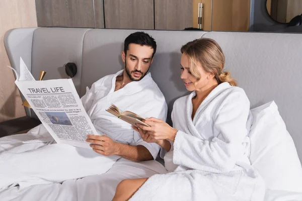 Mulher Sorridente Mostrando Livro Para Namorado Muçulmano Com Jornal Cama — Fotografia de Stock