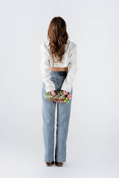 Back view of woman with flowers in sleeves of jacket standing on grey background 