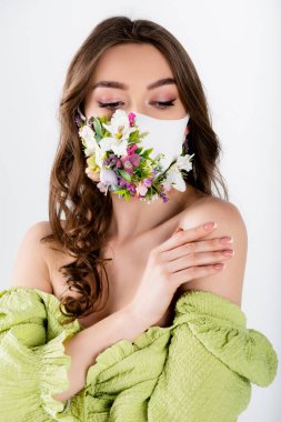 Tıbbi maskeli kıvırcık esmer kadın. Gri renkli çiçekleri var. 